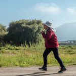 A woman in sportswear jogs along a rural road, surrounded by lush countryside and mountains.