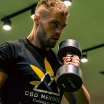 Muscular man exercising with a dumbbell in a modern gym setting, emphasizing strength and fitness.